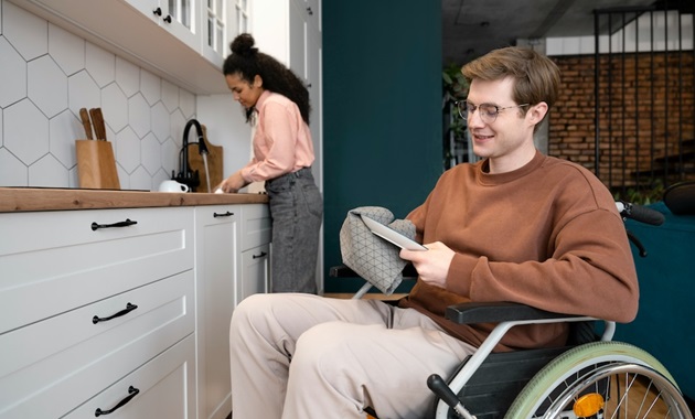 Man in wheelchair drying dishes while woman uses sink