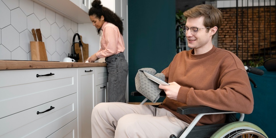Man in wheelchair drying dishes while woman uses sink