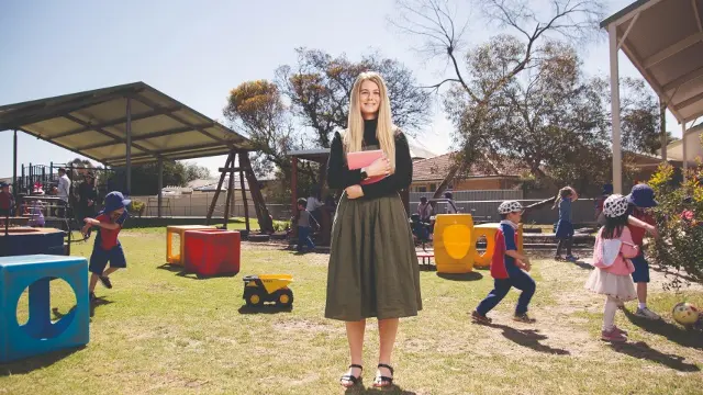 Primary school teacher standing in the playground surrounded by students