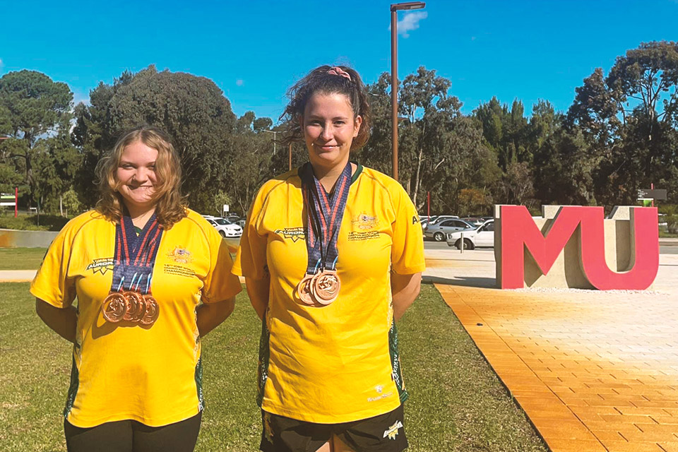 Two atheletes with medals standing next to the MU logo