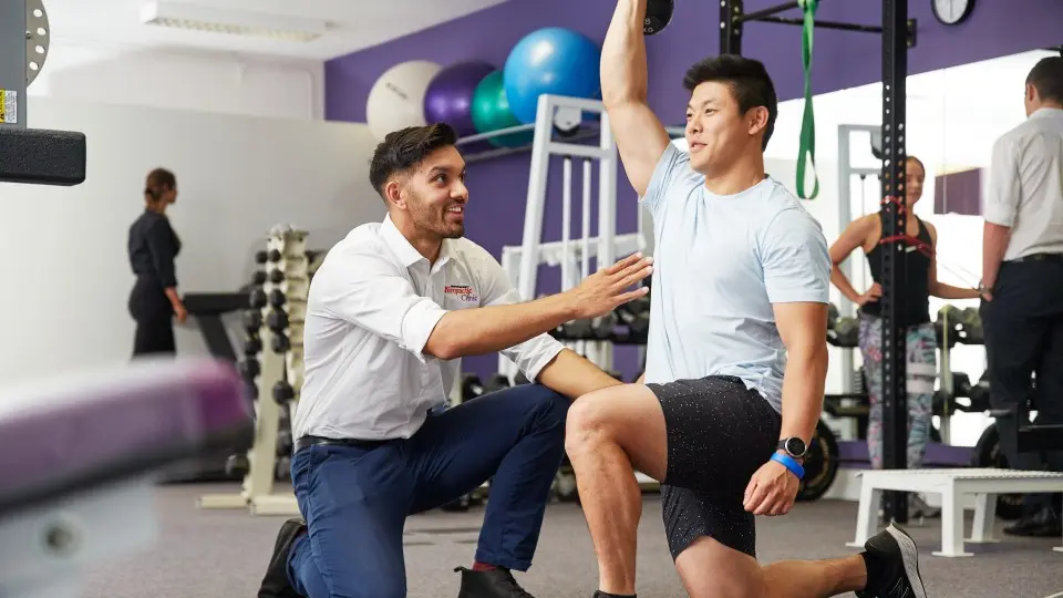 A chiropractic student assisting a patient with exercise in the gym.