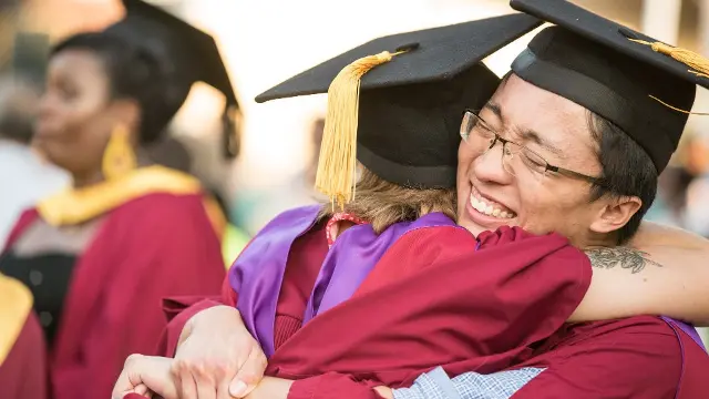 Male and female graduates hugging each other and smiling.