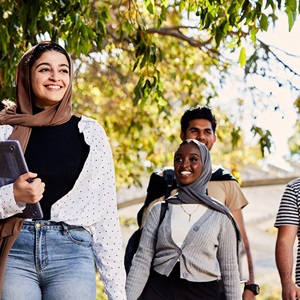 Group of students walking under a tree, smiling and looking happy.