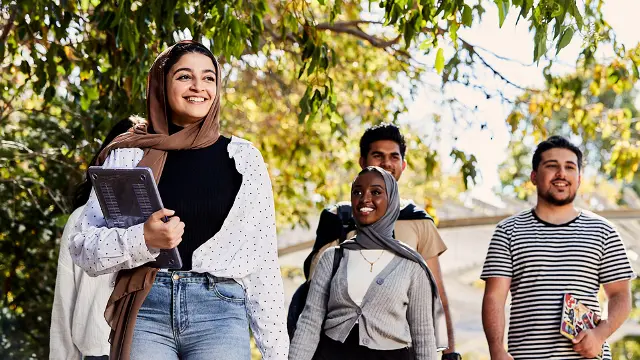 Group of students walking under a tree, smiling and looking happy.