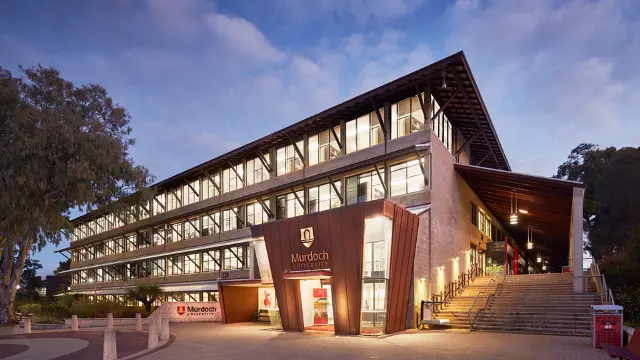 Murdoch University's South St campus at dusk, with brights lights still on and trees in the background.