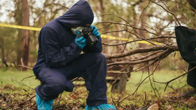 Forensics student in overalls taking photo of crime scene