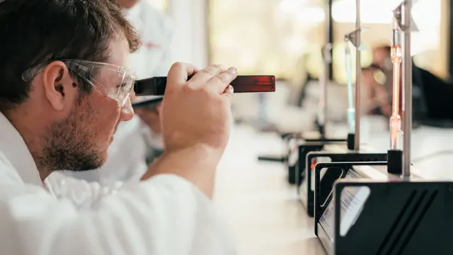 Science student examining equipment through safety goggles in a laboratory
