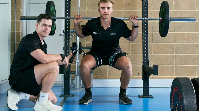 Allied health student coaching a client through a squat in a gym
