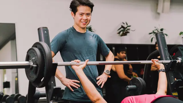 Allied health student assisting a client with a barbell exercise