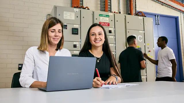 Engineering students reviewing work on a laptop at an electrical facility
