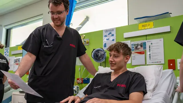 Nursing student and lecturer reviewing information at a patient bedside