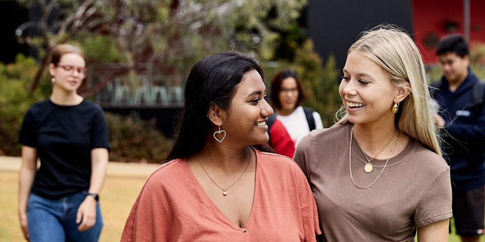 Two female students smiling with another in the backdrop