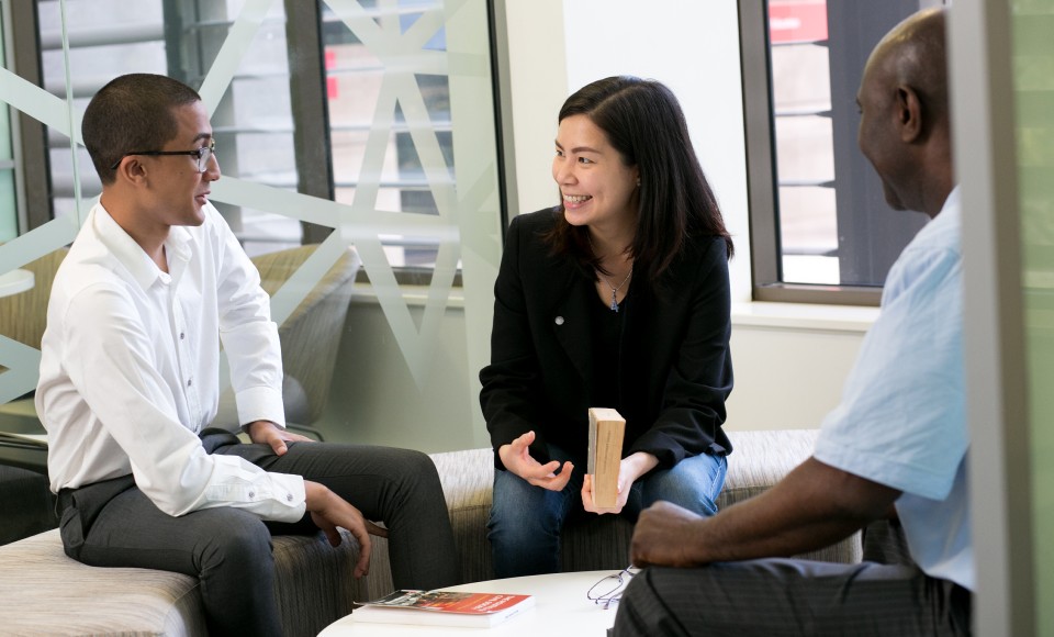 Two male and one female business students sitting on a circular bench indoors, talking.