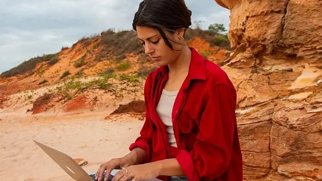 Murdoch University student with laptop outside with rock formation