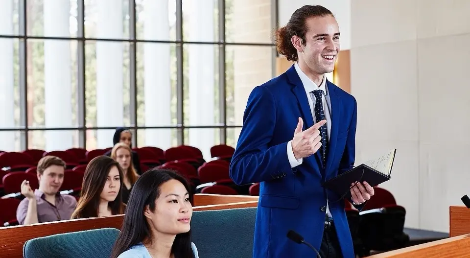 Murdoch University Law student presenting in moot court, holding book.