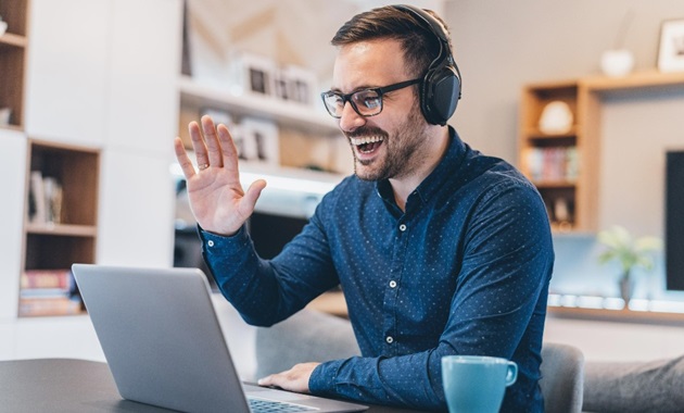 A man smiling and waving at someone via video chat.