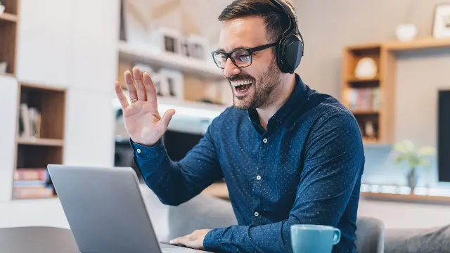 A man smiling and waving at someone via video chat.