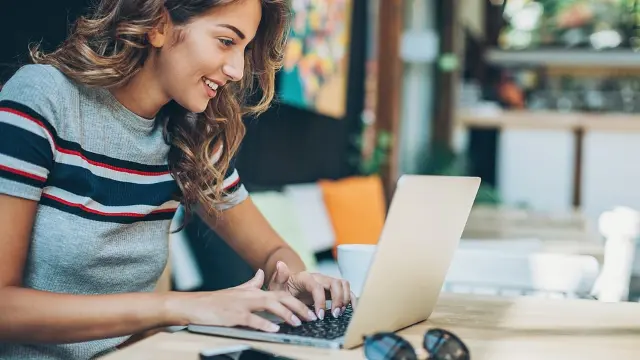 A woman sitting at a table, smiling and using a laptop.