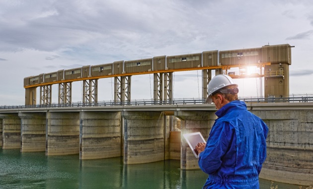 A surveyor in a reflective vest surveying water at a dam.