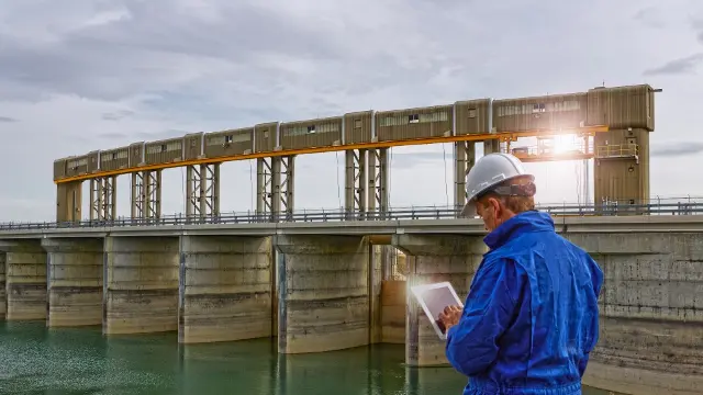 A surveyor in a reflective vest surveying water at a dam.