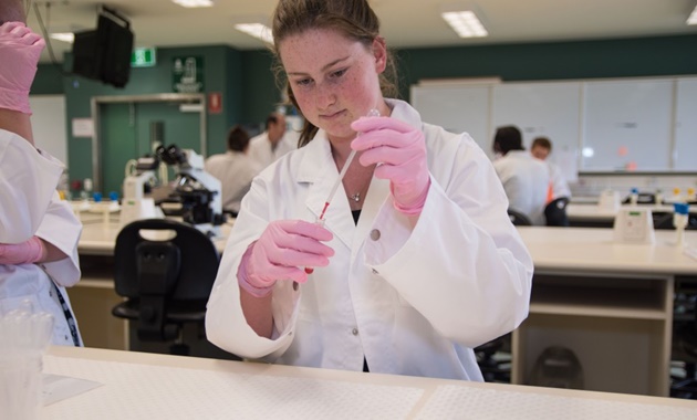 High school student working with a pipette in a science lab.