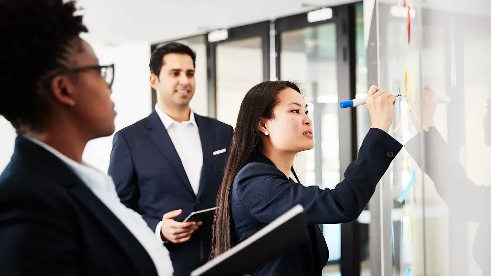 Three business students working together at a whiteboard.