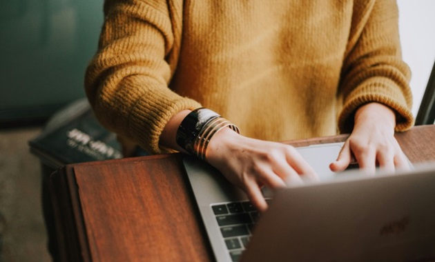 Person in yellow jumper works at a laptop.
