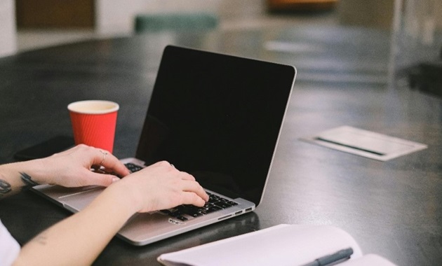 person using laptop with red coffee cup in background