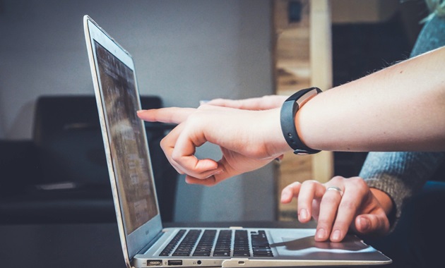 Two people's hands pointing and typing on a laptop