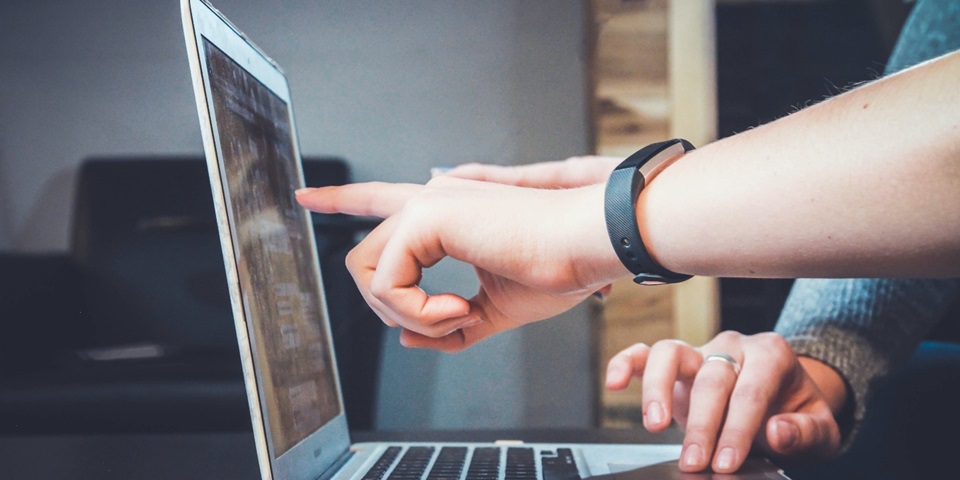 Two people's hands pointing and typing on a laptop