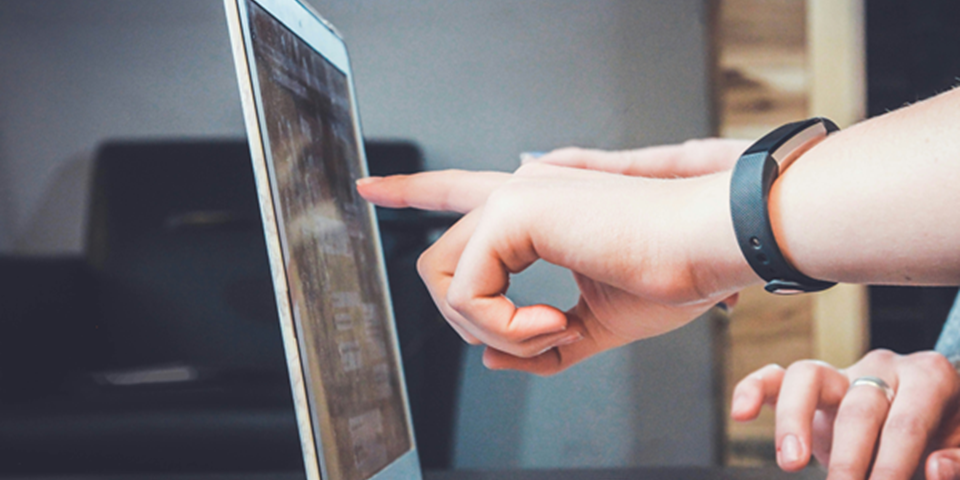 Two people's hands pointing and typing on a laptop
