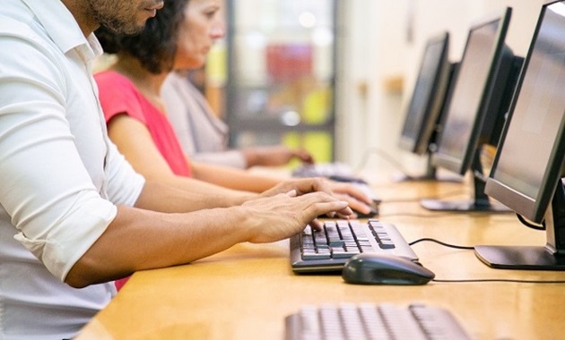 Three people sit, working at desktop computers.
