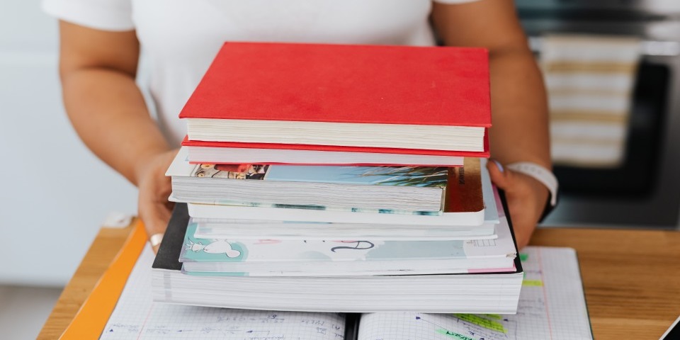 A person sets a pile of books on top of an open notebook.