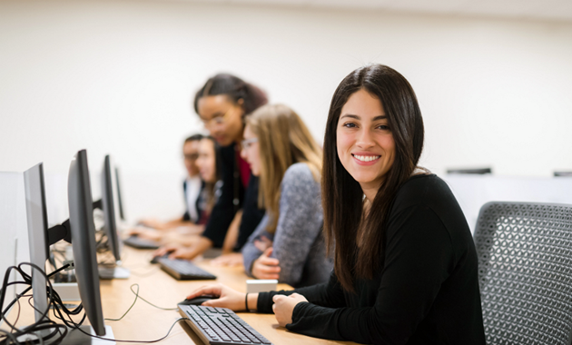 People sitting at desktop computers with one person smiling at the camera