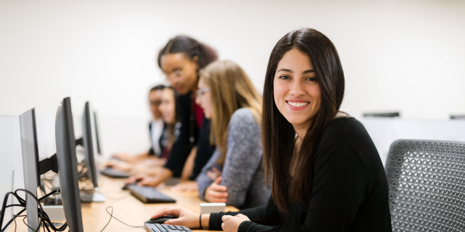 People sitting at desktop computers with one person smiling at the camera