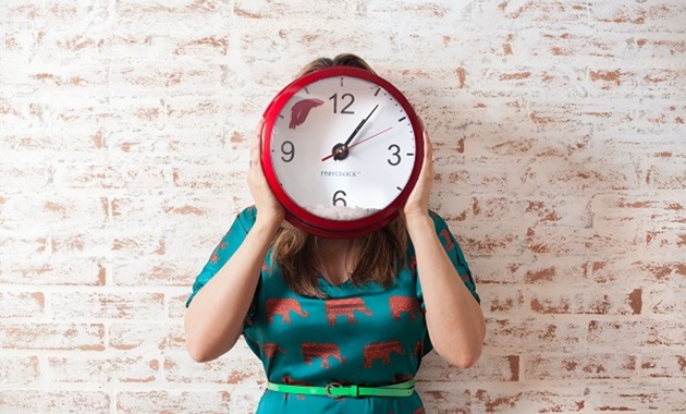 Woman in green dress holding up a red and white clock in front of her face.