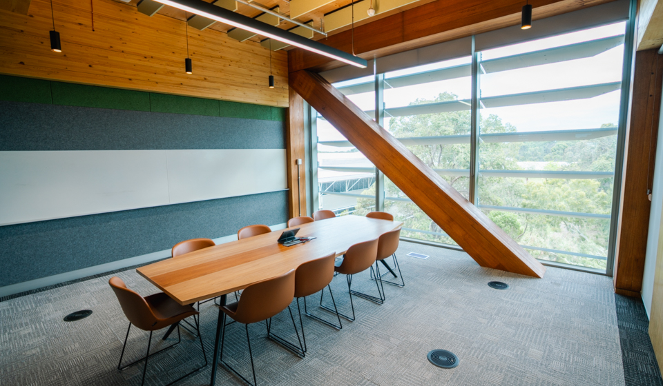 Room with large boardroom table and chairs, in front of large window and wooden beam