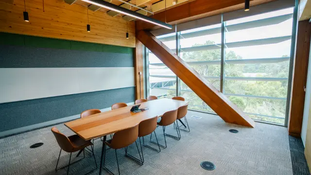 Room with large boardroom table and chairs, in front of large window and wooden beam