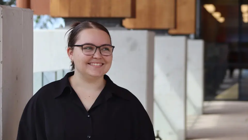 A smiling student stands in front of Boola Katitjin