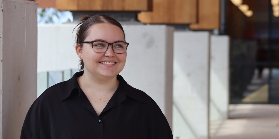 A smiling student stands in front of Boola Katitjin