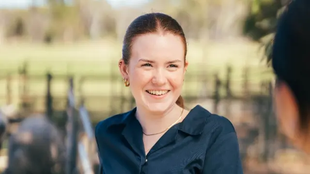 A smiling vet student holds onto a fence railing.