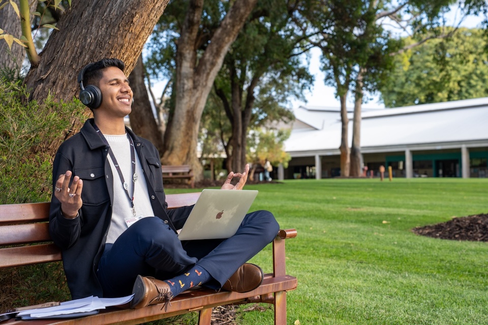 Student sitting on bush court meditating with laptop