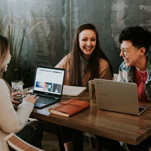 Three women working on laptops at a table, focused and engaged in their tasks.