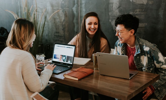 Three women working on laptops at a table, focused and engaged in their tasks.