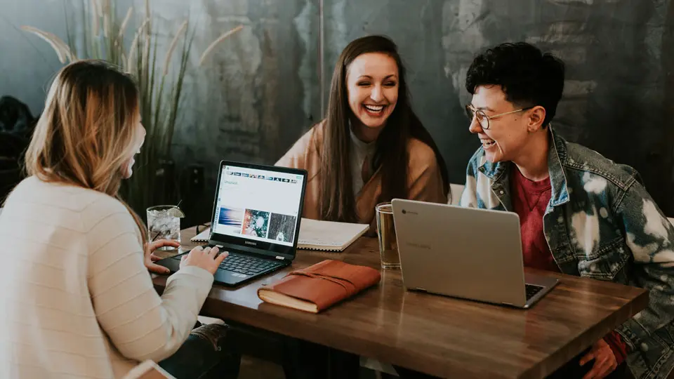 Three women working on laptops at a table, focused and engaged in their tasks.