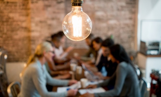 A group of people collaborating underneath a light bulb