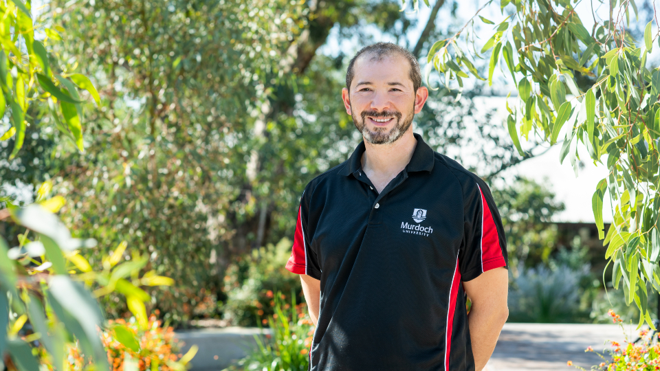 Aleks Nikoloski standing in front of greenery.