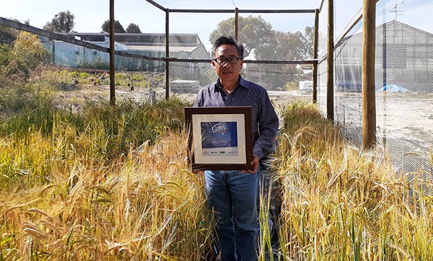 Chengdao Li holding his award near some barley