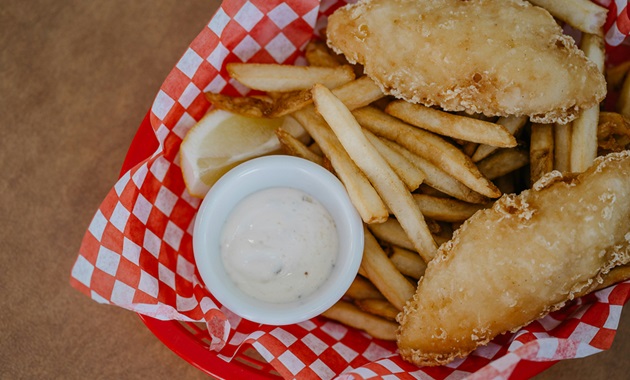 Fish and chips in a takeaway box with aioli.