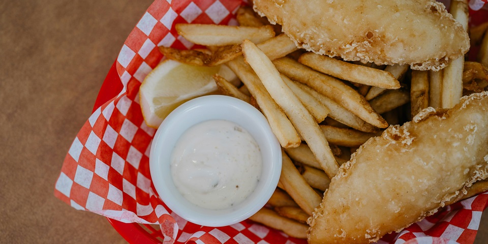 Fish and chips in a takeaway box with aioli.